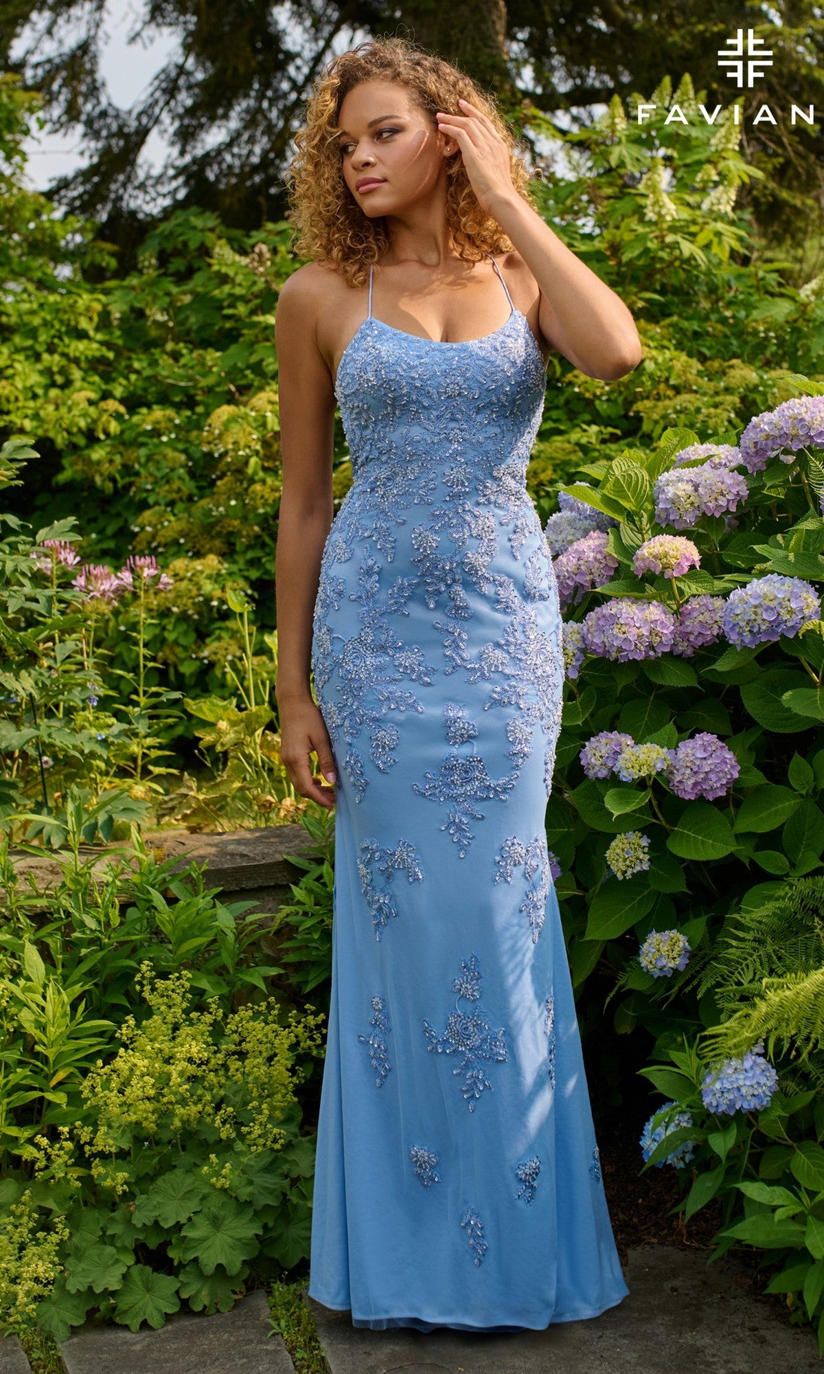 A woman wearing the Faviana 11440 long prom dress in fitted light blue with beaded applique stands outdoors among blooming hydrangeas and lush greenery.